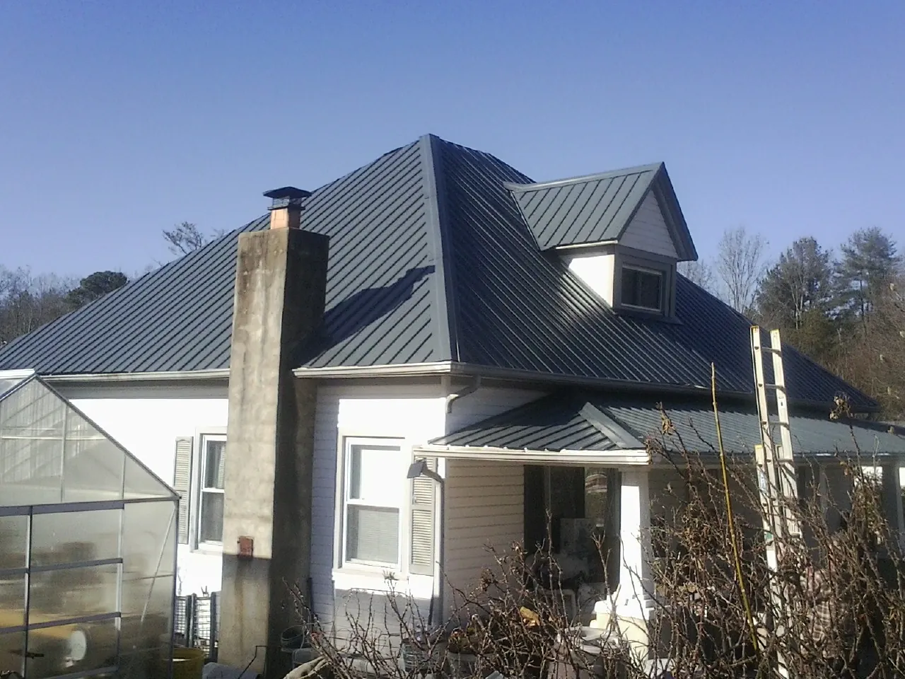 Dark blue standing seam metal roof on a white farmhouse with dormer — Slate & Tile Roof Repair by Roofing Brothers in Odenville
