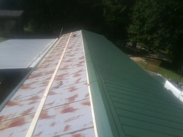 Old rusted panels beside newly installed green metal roofing — Wind Damage Roof Repair by Roofing Brothers in Odenville