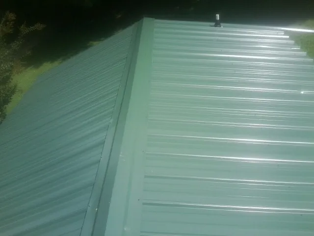 New green metal panels meeting at the ridge of a roof — Flat Roof Repair work by our crew in Odenville