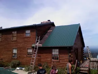 Green metal roof going on a two story log home with ladders set in Odenville