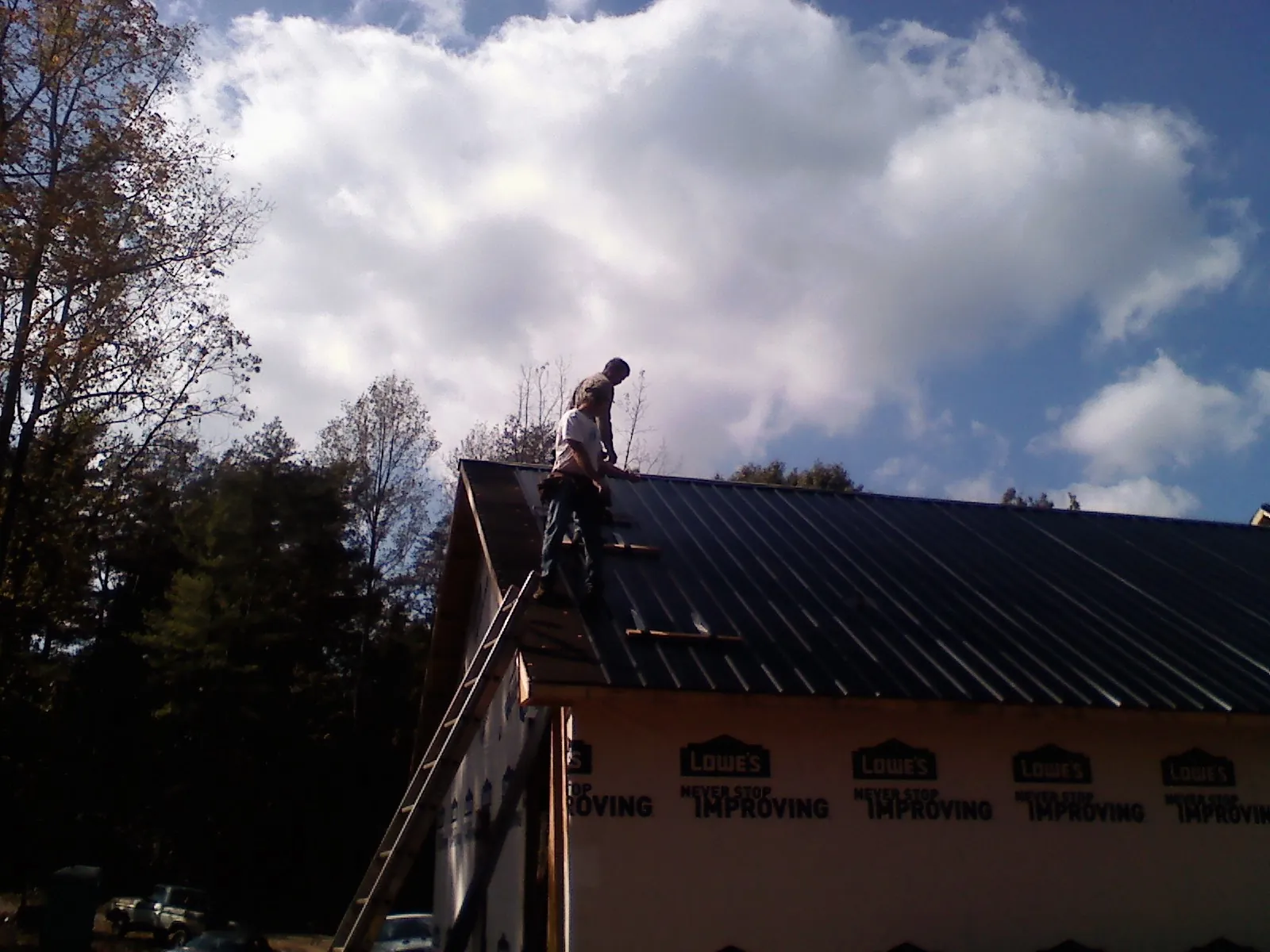 Roofer fastening dark metal panels high against a cloudy sky, from a Roof Inspection job in Odenville
