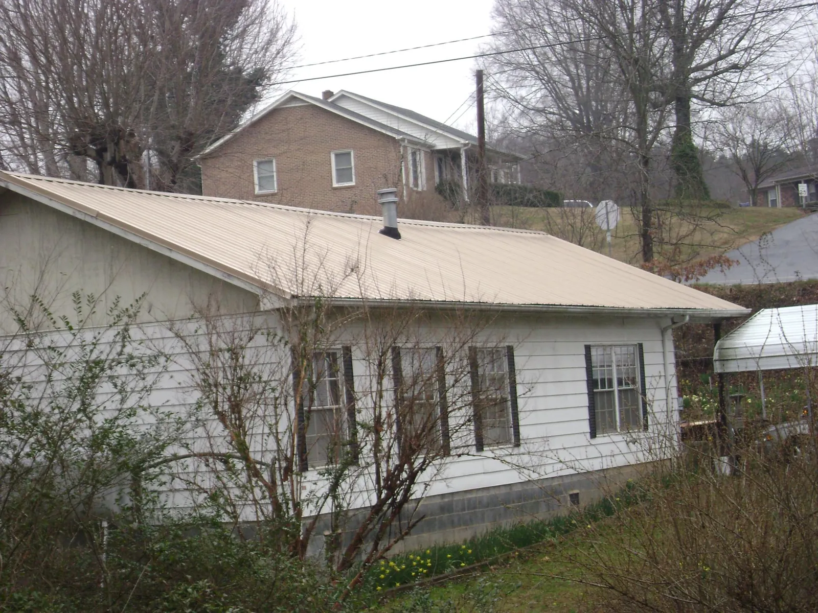 Tan metal roof on a white sided house set into a hillside — Commercial Roofing by Roofing Brothers in Odenville