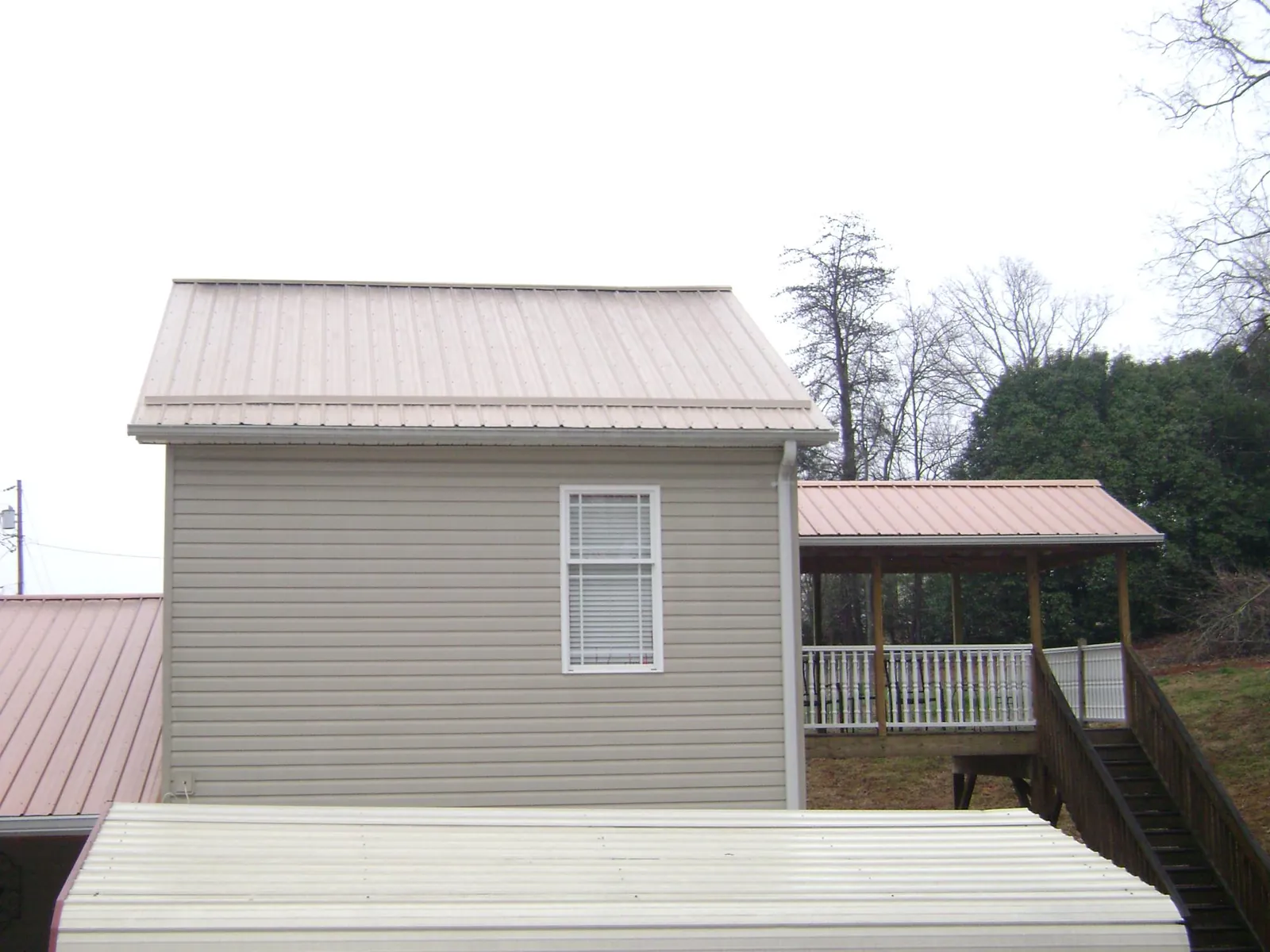 Tan metal roofs on a two story addition and attached porch, from a Roof Replacement job in Odenville